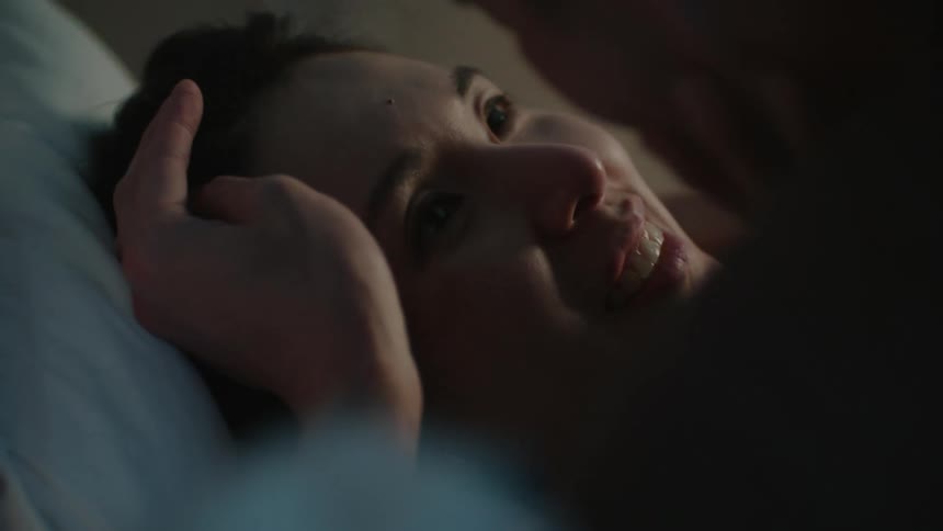 Man kisses the forehead of her wife while laying on the bed