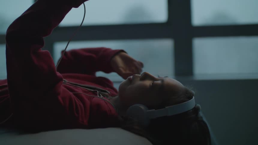 Girl wearing headphones talks on her smartphone laying on the bed at home