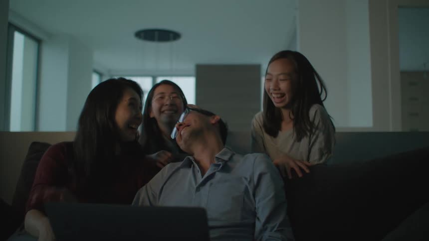 Family sitting on the couch in the living room at home laughing while looking at a laptop