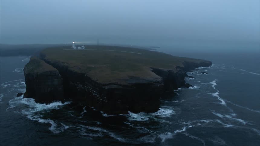 A lighthouse shines out from a small island in the ocean