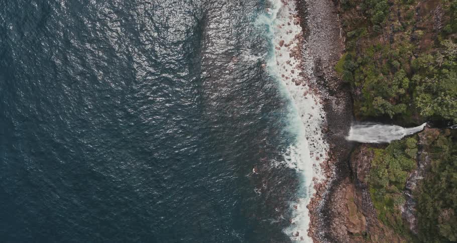 Aerial view of sea waves breaking against the shore with waterfall and forest