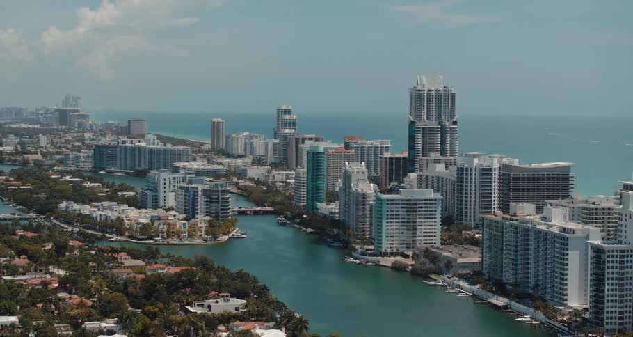 Buildings and trees next to the ocean with the sky and clouds in the background
