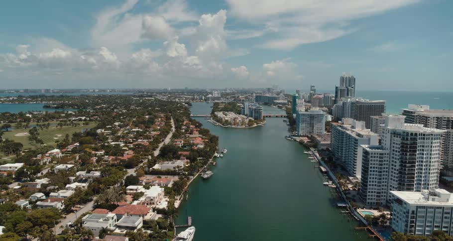 Boats are docked on both sides of a canal with tall buildings on one side and neighborhood homes on the other