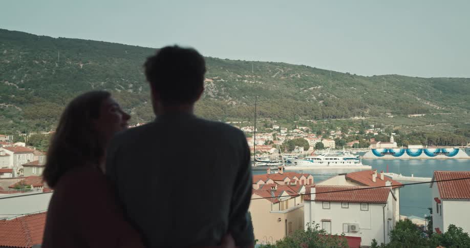 Two people overlooking harbor town from a balcony and pointing towards the lake
