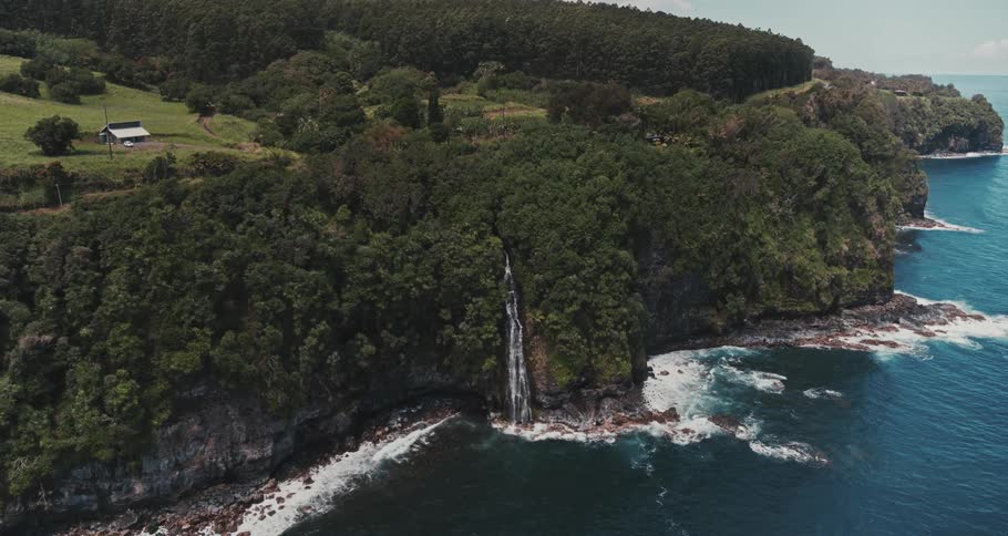A waterfall surrounded by lush trees is flowing down a rock cliff into the ocean