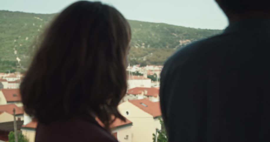 A woman leans in to kiss her boyfriend as they stand on their balcony