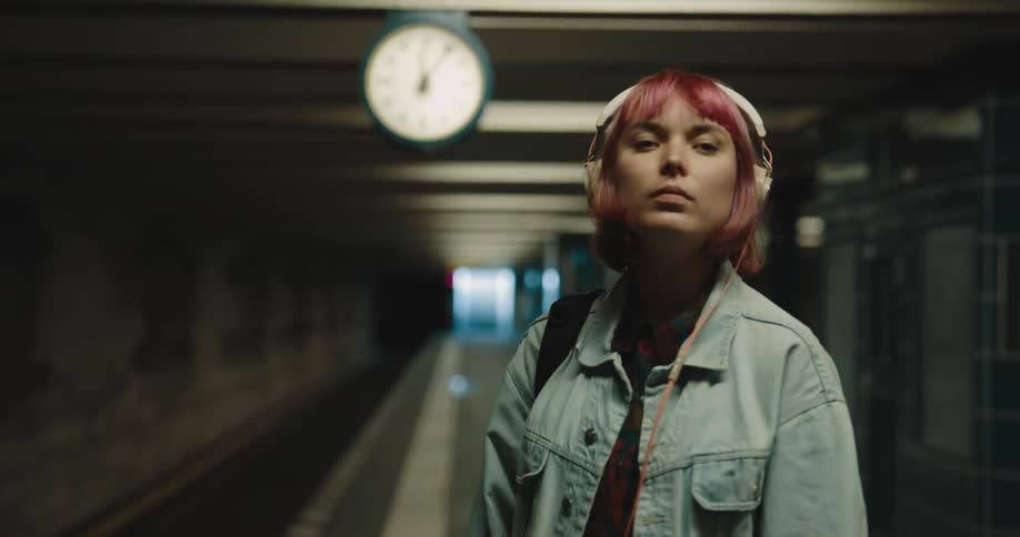 A woman wearing headphones is nodding head to music while waiting in the subway