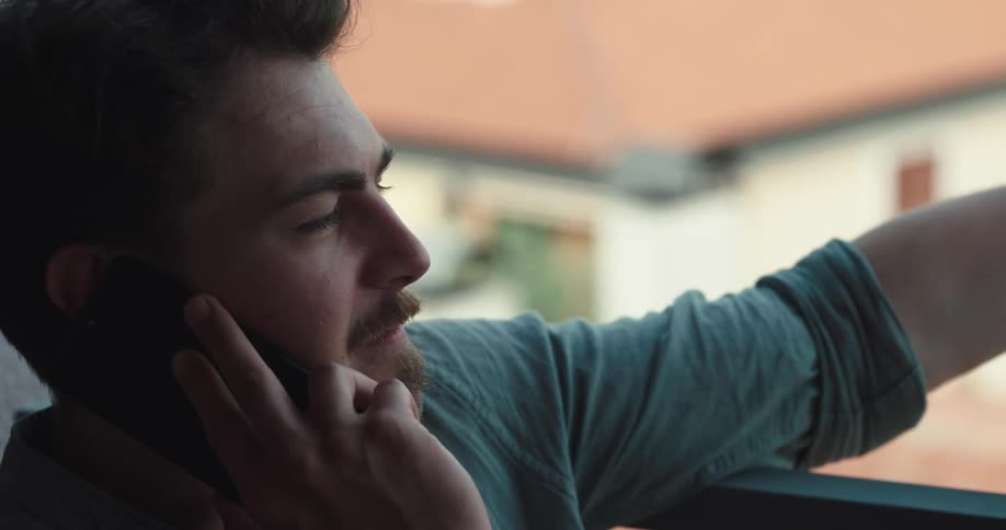 Man leans against balcony rail while talking on mobile phone with a smile