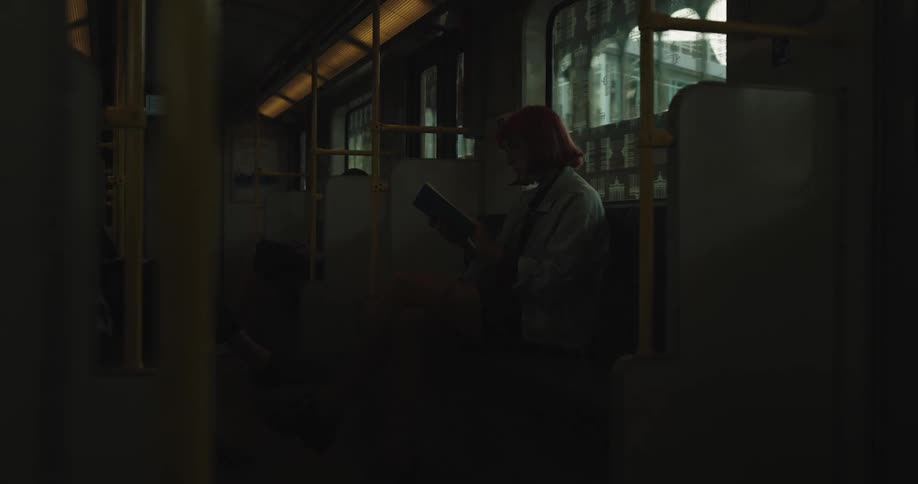 A young woman is sitting and reading a book while riding the subway