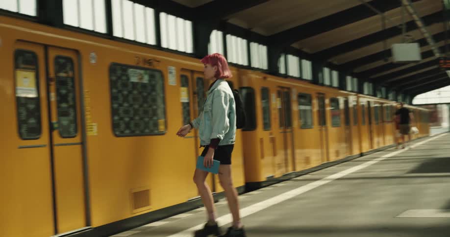 A girl with wine colored hair sitting on a bench gets up and walks to the train and goes inside
