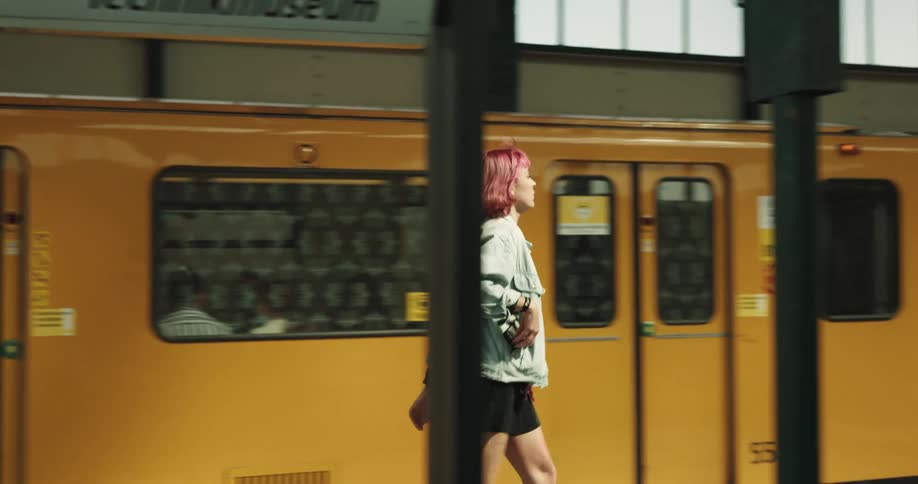 Woman with pink hair denim jacket and black shorts gets off yellow train