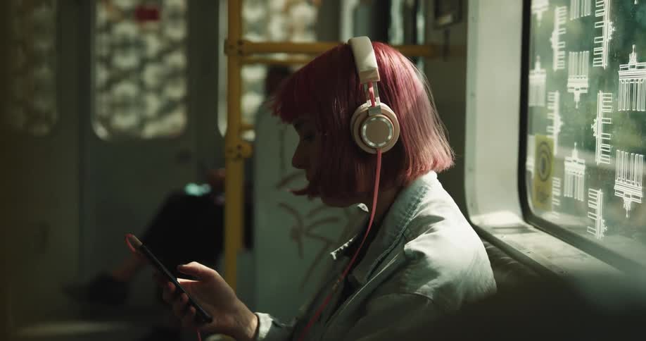 A woman puts on headphones to listen to music on her phone while on a train