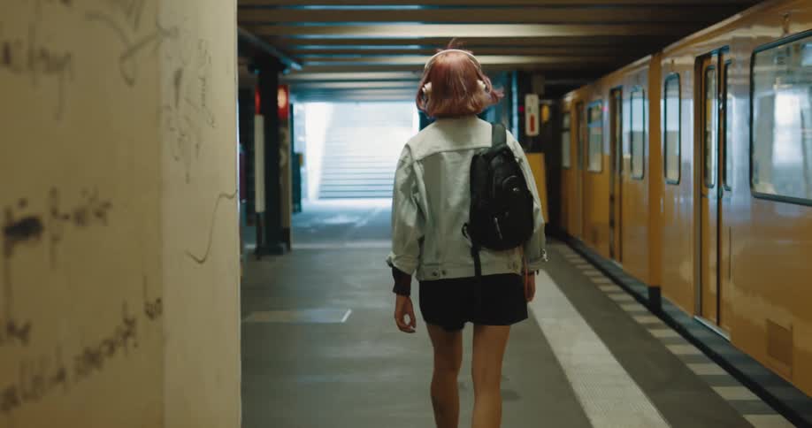 A woman is walking next to a subway train towards stairs that lead to ground level