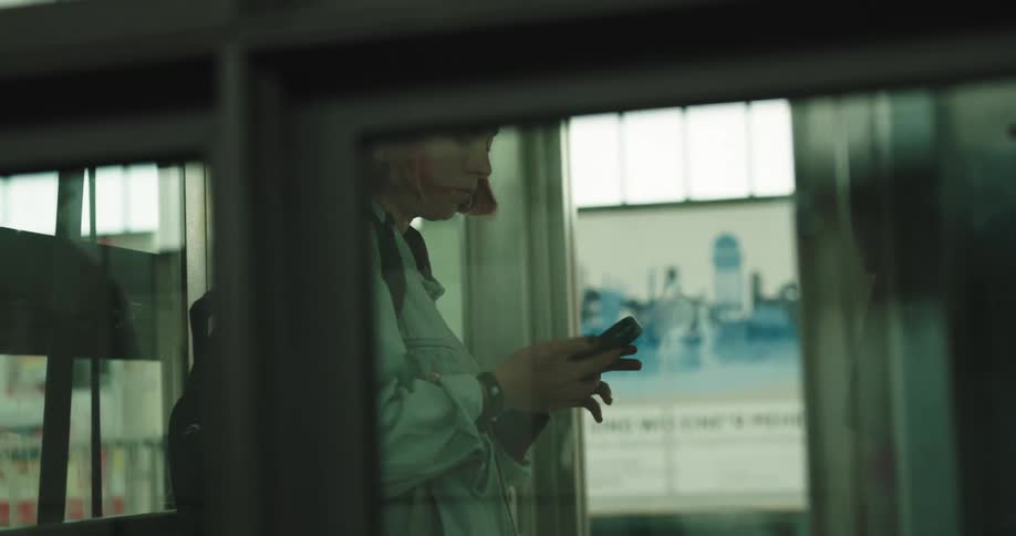 A woman walks into a glass elevator then looks at her phone