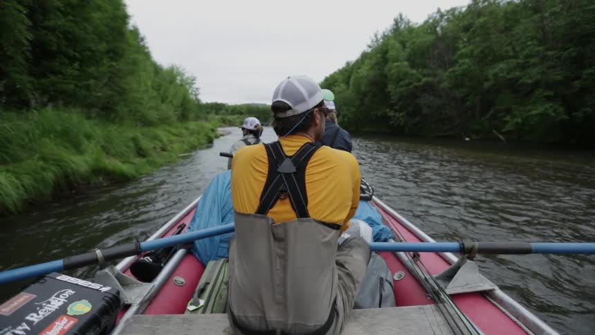 Fishermen float down a tree-lined river