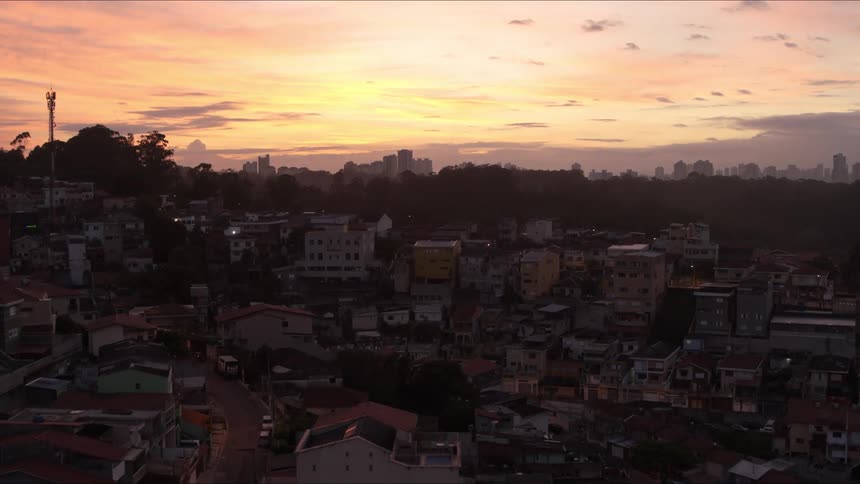 Tree covered hill separates peripheral neighborhood from city under red tinted sky