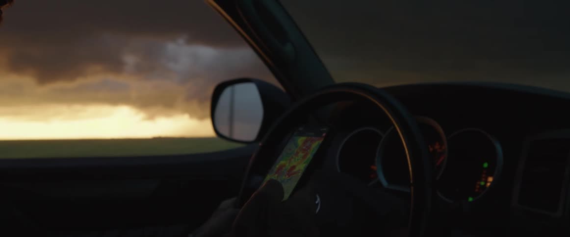 A person in a vehicle looking at a smart phone with the sky and clouds in the background