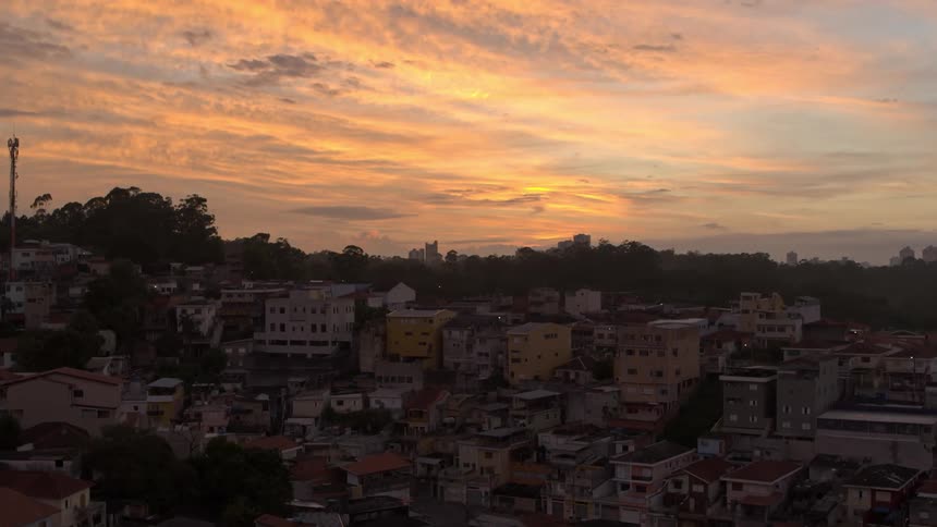 A crowded peripheral neighborhood with tall buildings looming on the horizon under a colorful sky