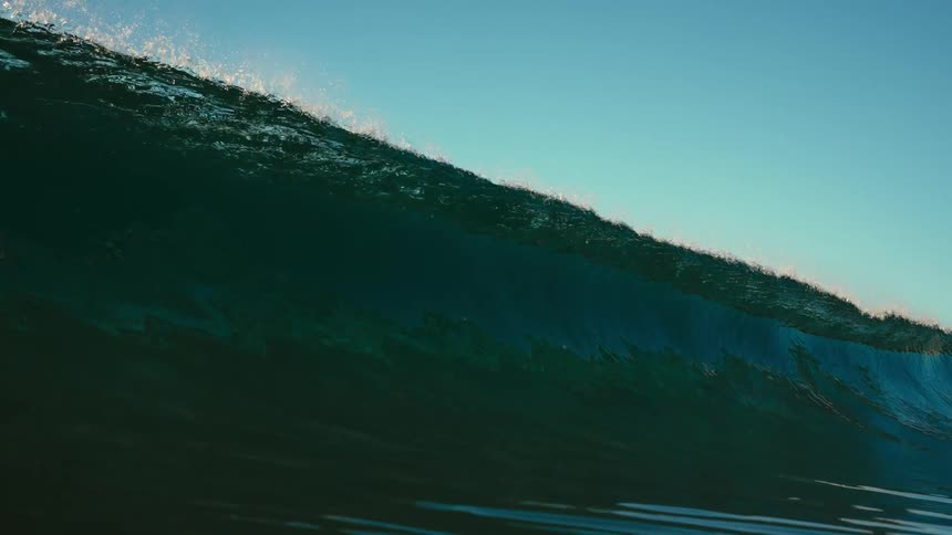 Large wave rolls and crashes onto surface reflecting sunlight