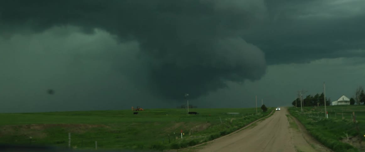 A dirt road with a vehicle with a storm the sky and clouds in the background