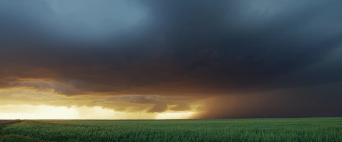 A storm is passing over wide open farmland with rain and lightning in the distance