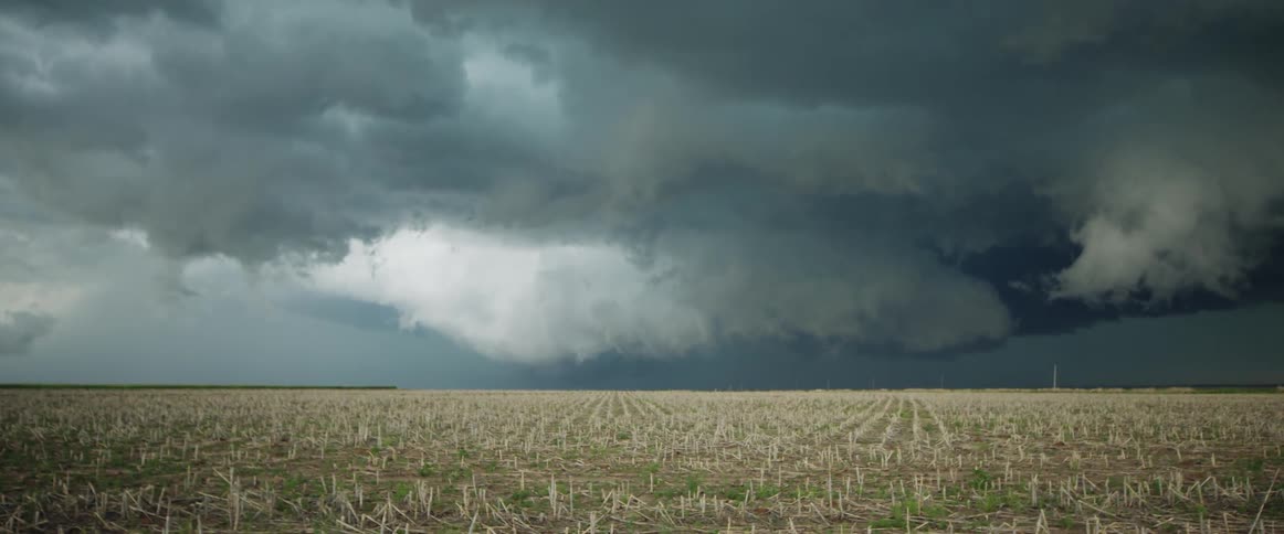 A landscape with a grassy field with a storm the sky and clouds in the background