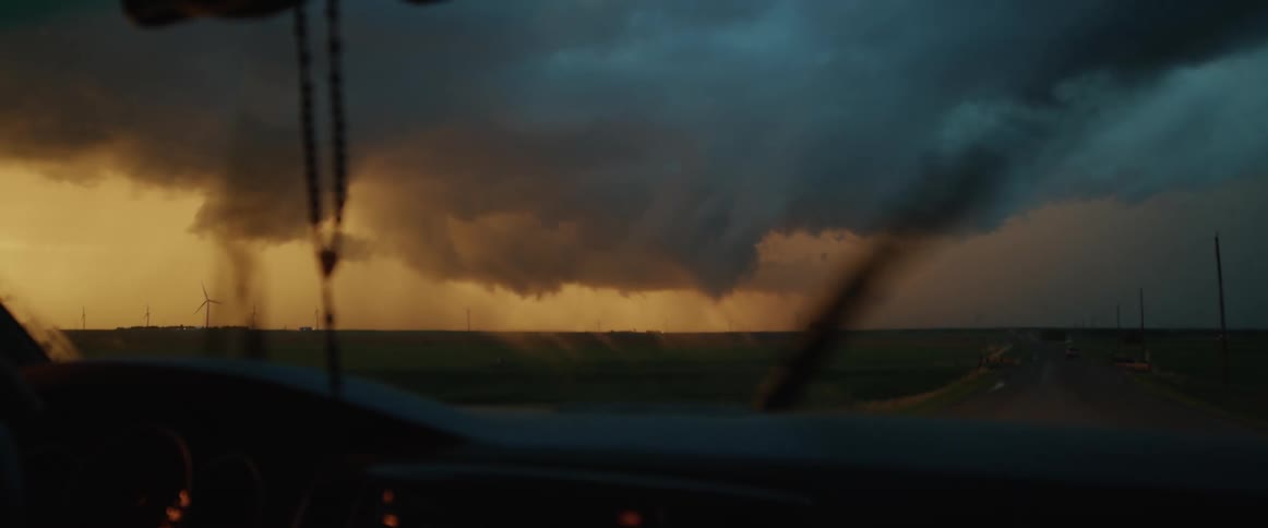 Windshield wipers work as car approaches vehicle on highway and lighting strikes in storm clouds over wind farm