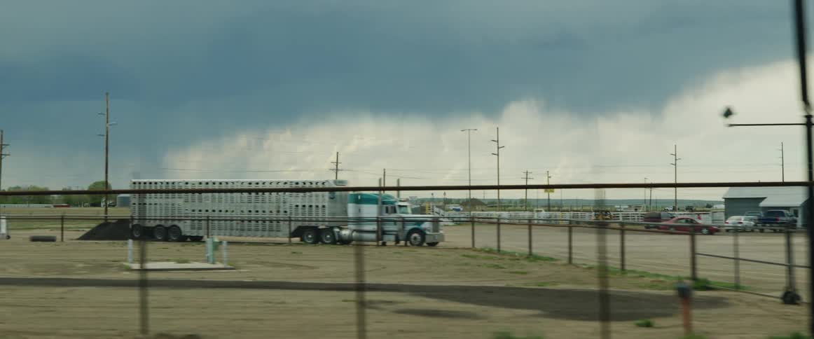Passing by a rodeo events facility with parked trucks and campers during the day with distant rain in the background