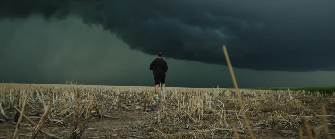 A man with a camera walking on a landscape with a storm the sky and clouds in the background