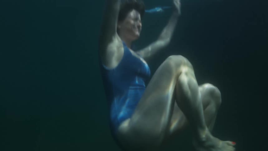Woman swims underwater kicking before rising toward surface