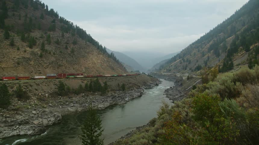 A small river flows through a valley on a foggy day with a motionless freight train in the background