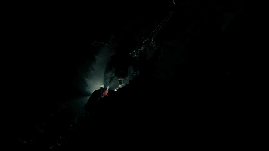 A man in a cave with a light on his head looks around as he sets up camp