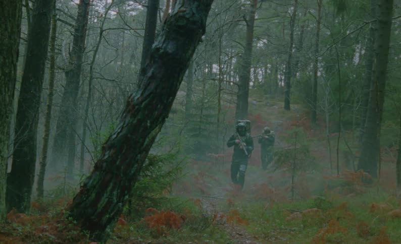 Camouflaged soldiers move alertly through foggy woods with their weapons ready