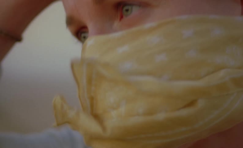 A woman wearing a yellow bandanna over her nose and mouth pushes her hair back from her face in the wind