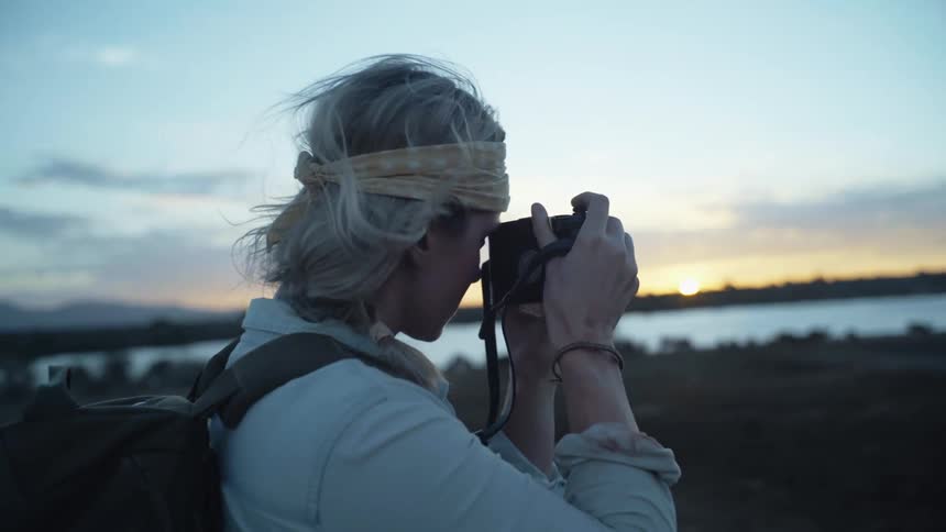 A person holds their camera up to photograph the sunset over the water