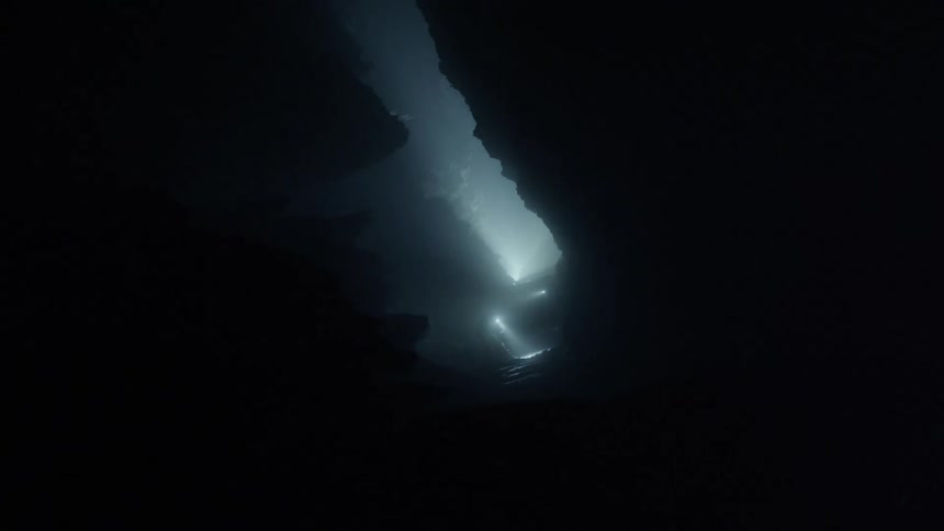 A person with a flashlight by the entrance of a cave