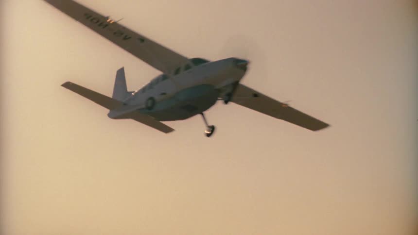 An airplane flies over desert mountains in a hazy yellow sky