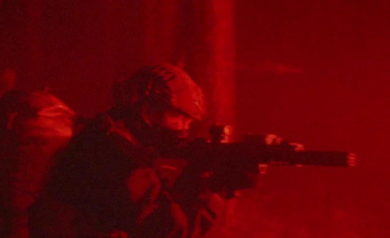 Soldier with their guns raised walk through a forest and look around at night