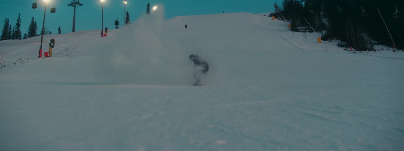 Snowboarder rides snowboard down snowy slope as ski lift operates behind them