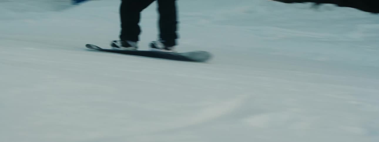 Snowboarder rides down snowboarding course toward buildings