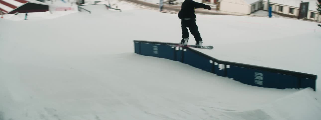 A snowboarder almost falls trying to spin off a rail on a mountain