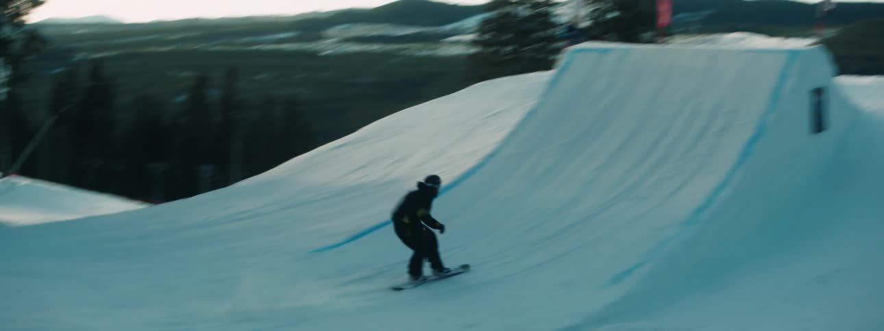 A person snowboards down the slope and jumps off a ramp