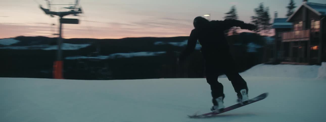 A snowboarder weaves and turns as he passes under the ski lift