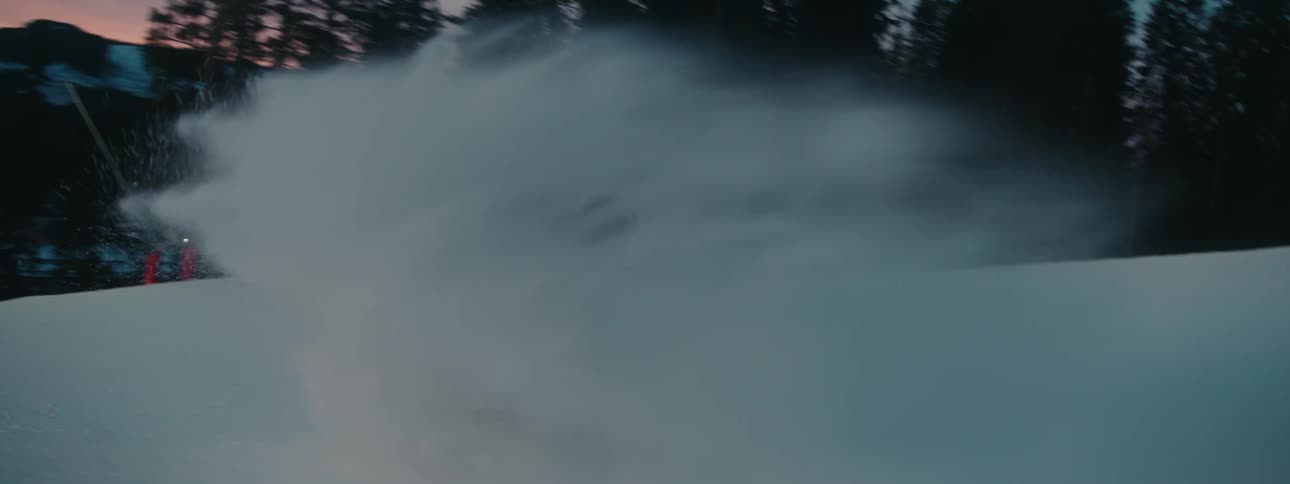 A snowboarder kicks up snow to slow his speed as he accelerates down the slope