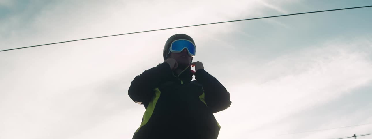 A skier adjusts their helmet while standing beneath a ski lift
