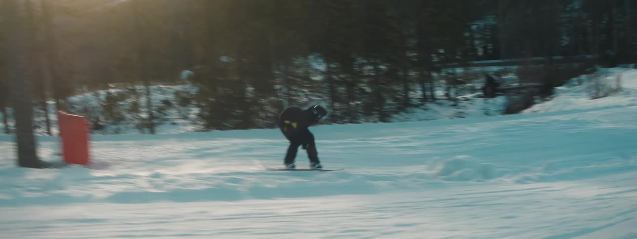 Snowboarder takes jump on course passing conifer trees