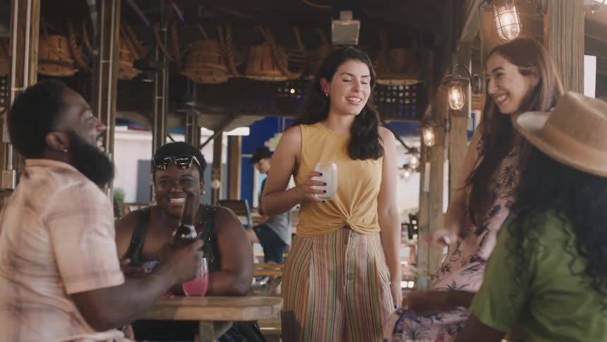 A group of friends talk and laugh while drinking at an outdoor restaurant