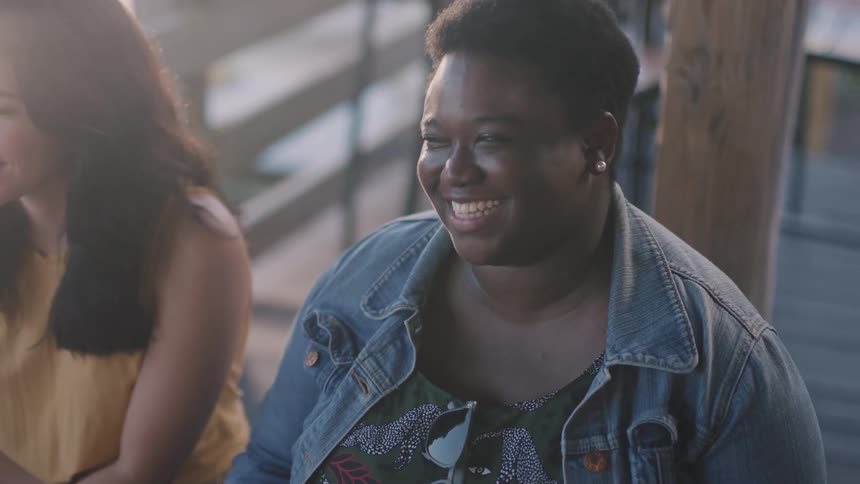 A woman shakes her head and laughs while sitting with others outdoors during the day