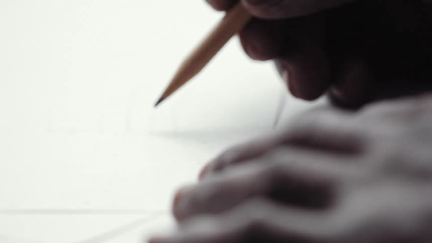 A man holds down paper with one hand as he starts to use a pencil with the other hand