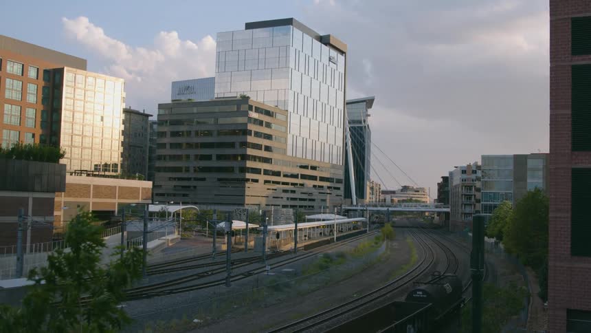 A train running on train tracks with buildings the sky and clouds in the background
